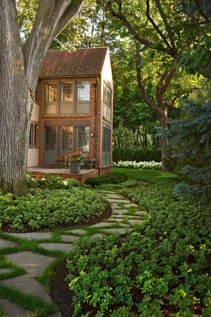 Wonderful-mass-of-green-plants-along-the-stone-path-alos-shady-trees-toward-the-brick-house-with-concrete-terrace-and-flower-in-pot