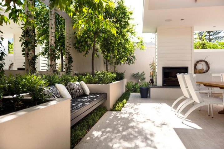 cozy-white-modern-patio-with-shady-bench-and-delightful-dining-space-decorated-by-mirrors-and-green-vines-also-stylish-fireplace-design